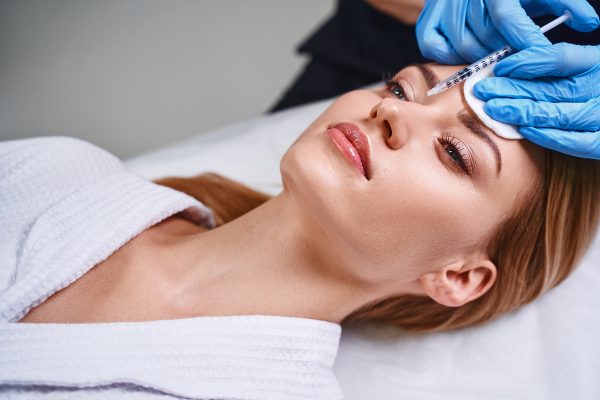 Young woman is preventing from age problems and visiting cosmetologist for using botox into forehead